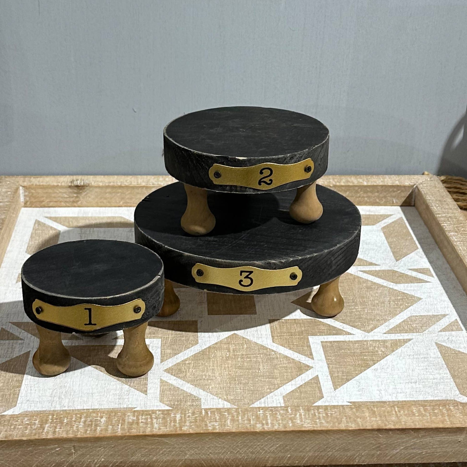 Set of 3 black round display risers with wooden legs, numbered 1 to 3. Solid wood construction, perfect for showcasing candles, plants, and decor.
