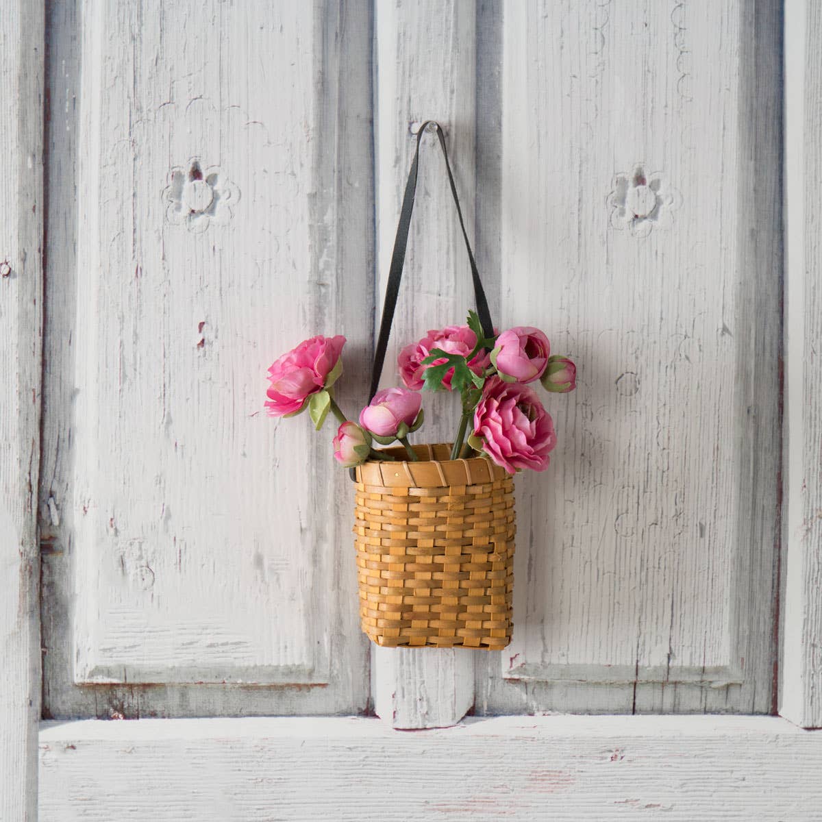 Oval Chipwood Hanging Planter with pink flowers, hung on a vintage wooden door. Rustic woven basket with leather strap for stylish home decor.