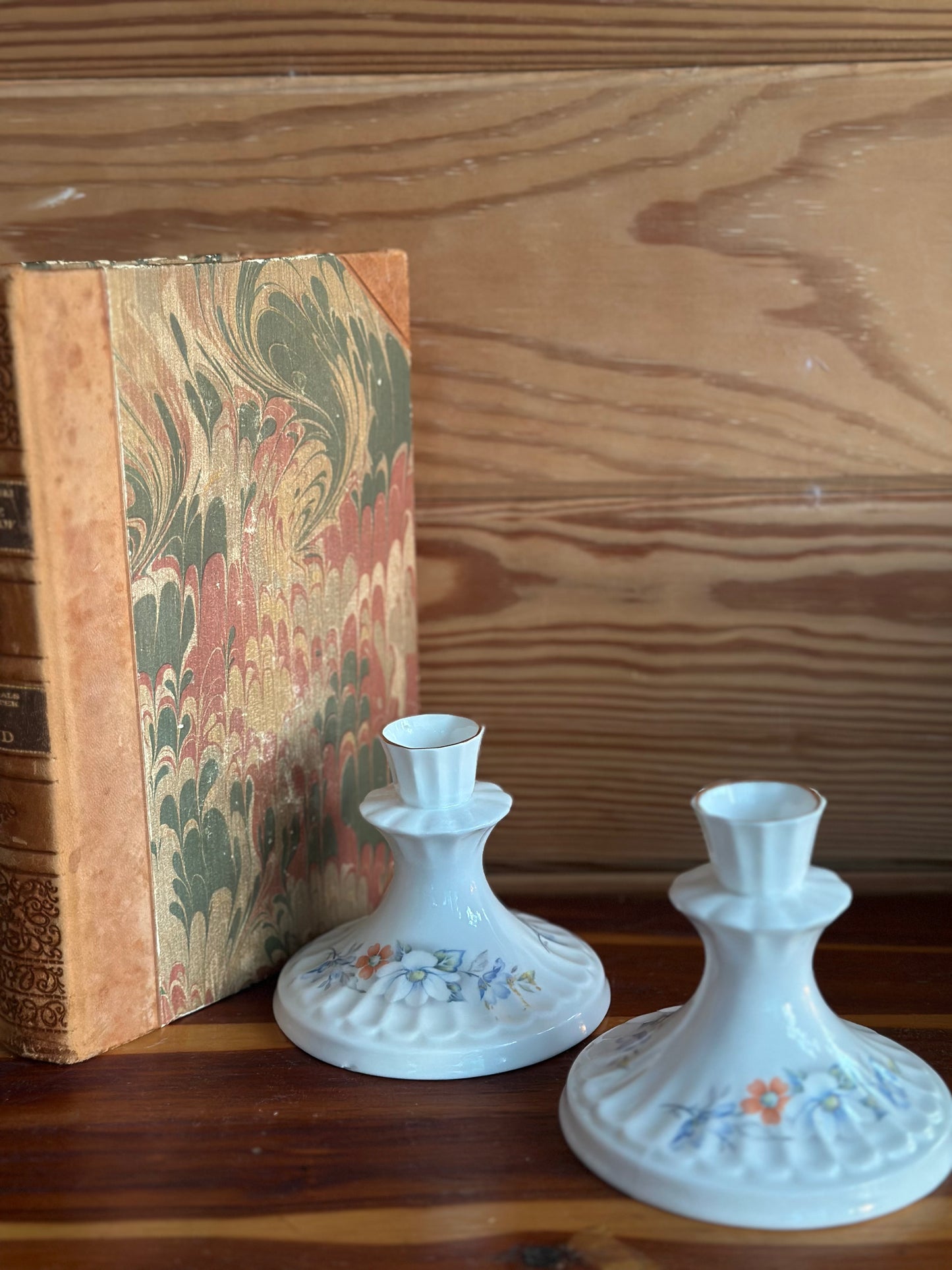 Pair of Vintage Royal Stewart candlesticks with floral motifs, displayed beside an antique book. Fine bone china for sophisticated decor.