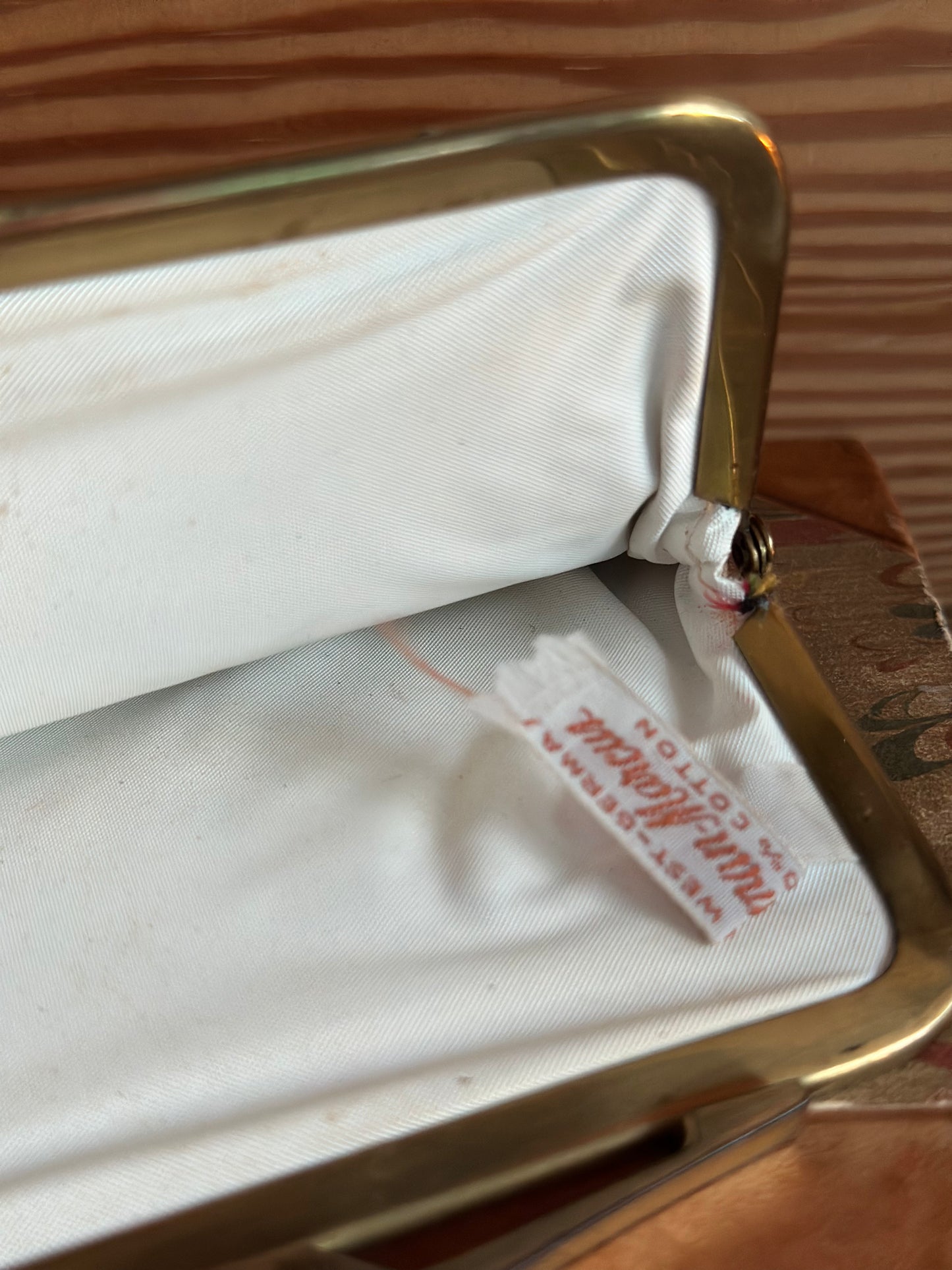 Interior view of vintage Neiman Marcus coin purse, revealing white satin lining and original label, framed by a sturdy brass clasp.