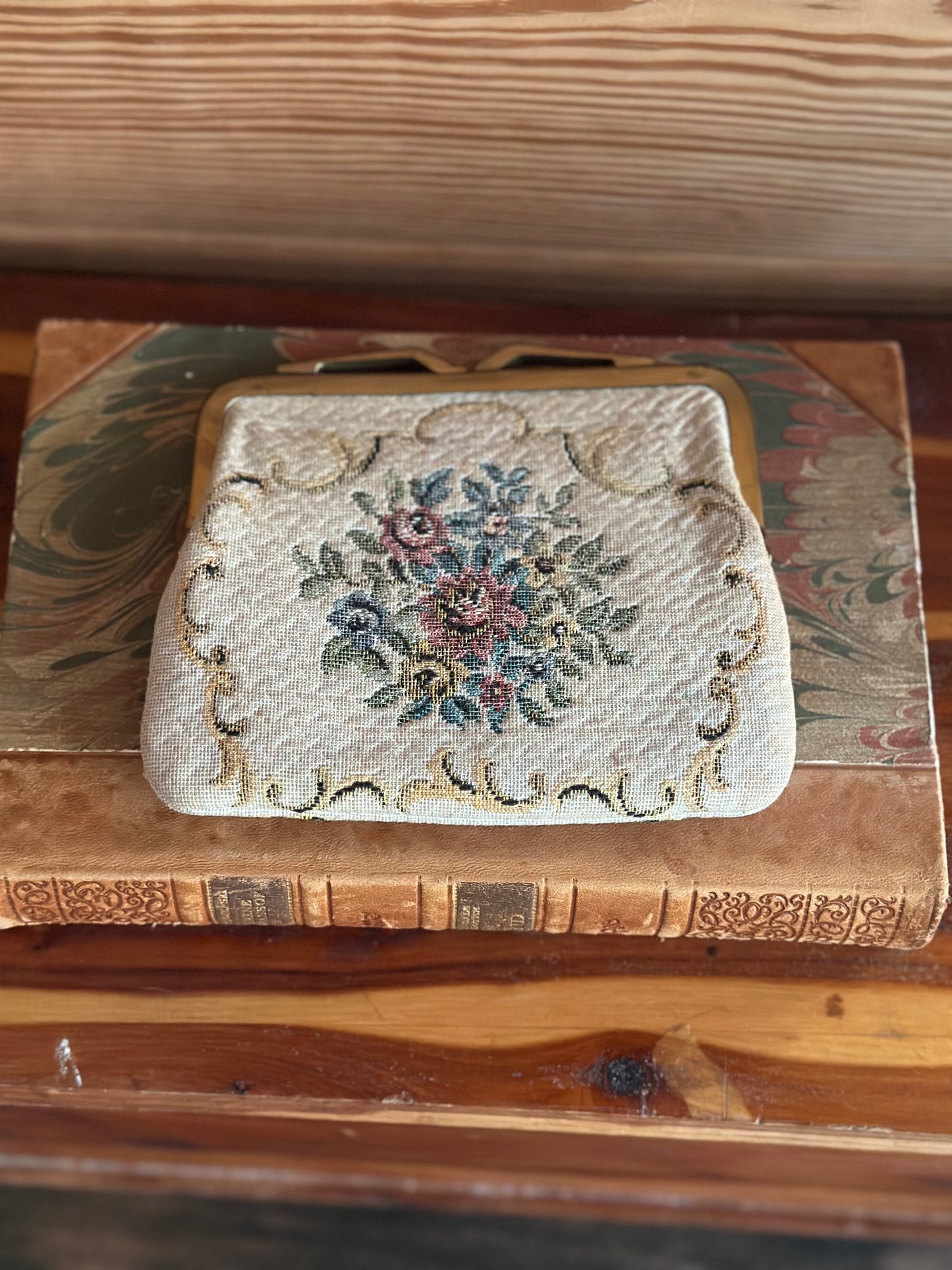 Antique-style 1950s floral tapestry coin purse resting on a vintage book, highlighting its timeless elegance and intricate embroidered details.