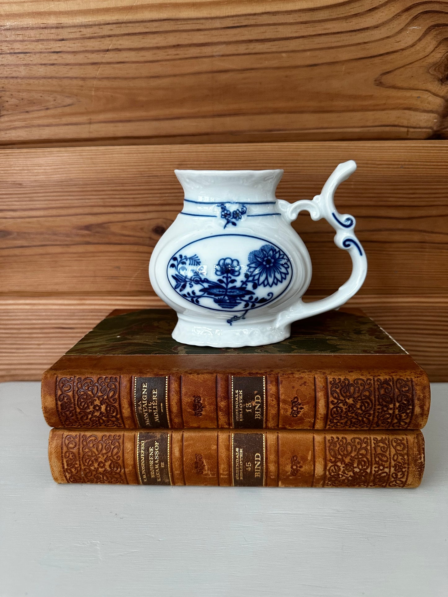 Classic vintage porcelain sipping cup from Karlovy with blue and white floral patterns, placed atop antique books for a timeless aesthetic.