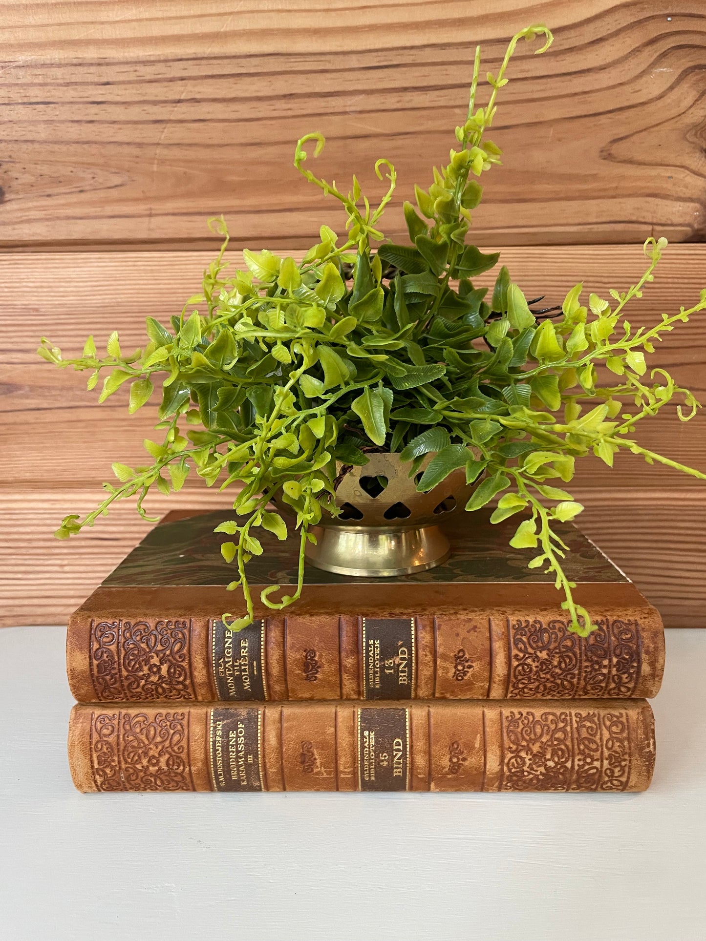 Vintage brass basket with heart-shaped cutouts, repurposed as a planter atop antique books. Handcrafted in India, perfect for home decor.