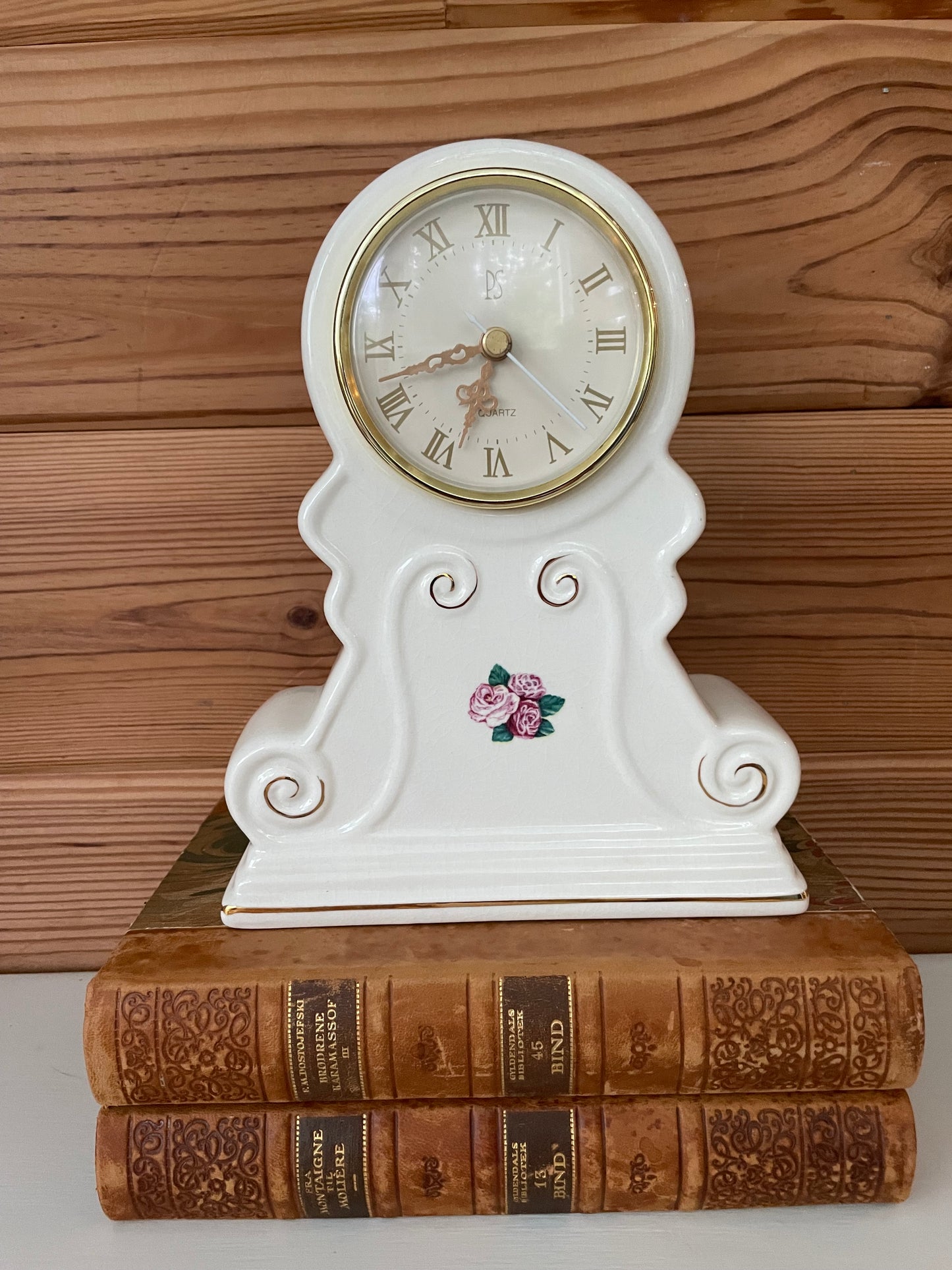 Limited edition 1998 vintage white porcelain mantel clock with gold-tone details, elegantly displayed atop antique leather-bound books.