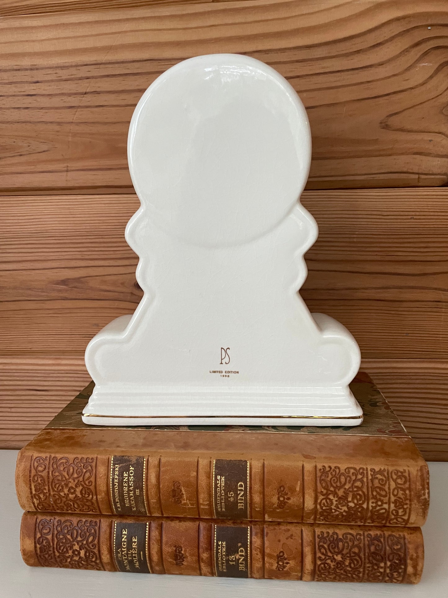 Back view of the vintage white porcelain mantel clock, showcasing its smooth finish and limited edition marking, resting on antique books.