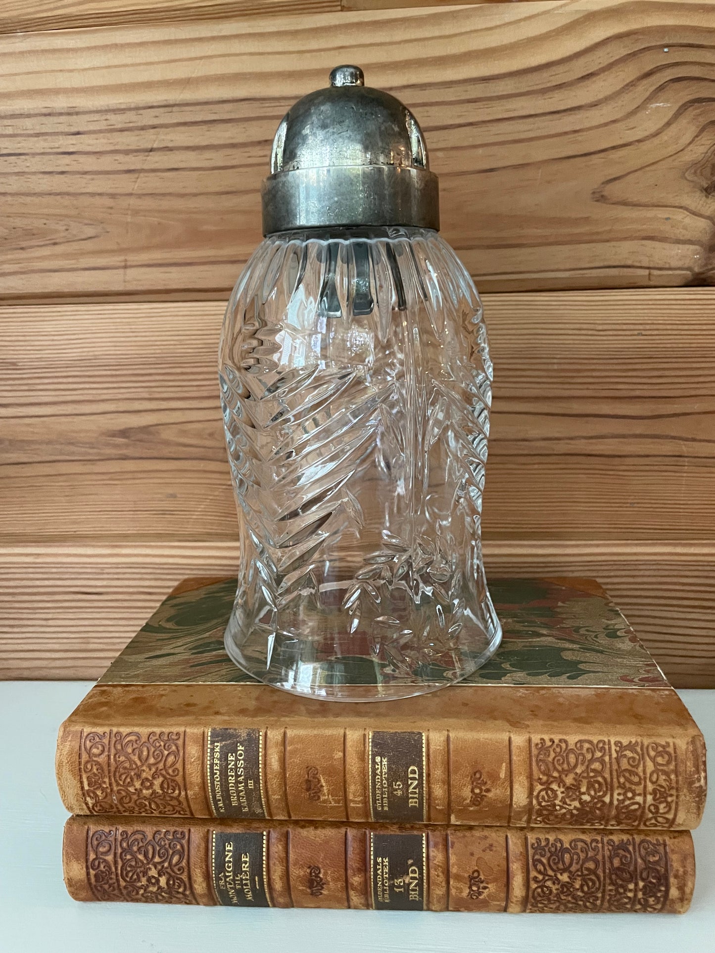 Elegant vintage glass hurricane cloche with a metal top, resting on antique books. A perfect decorative piece for classic home interiors.