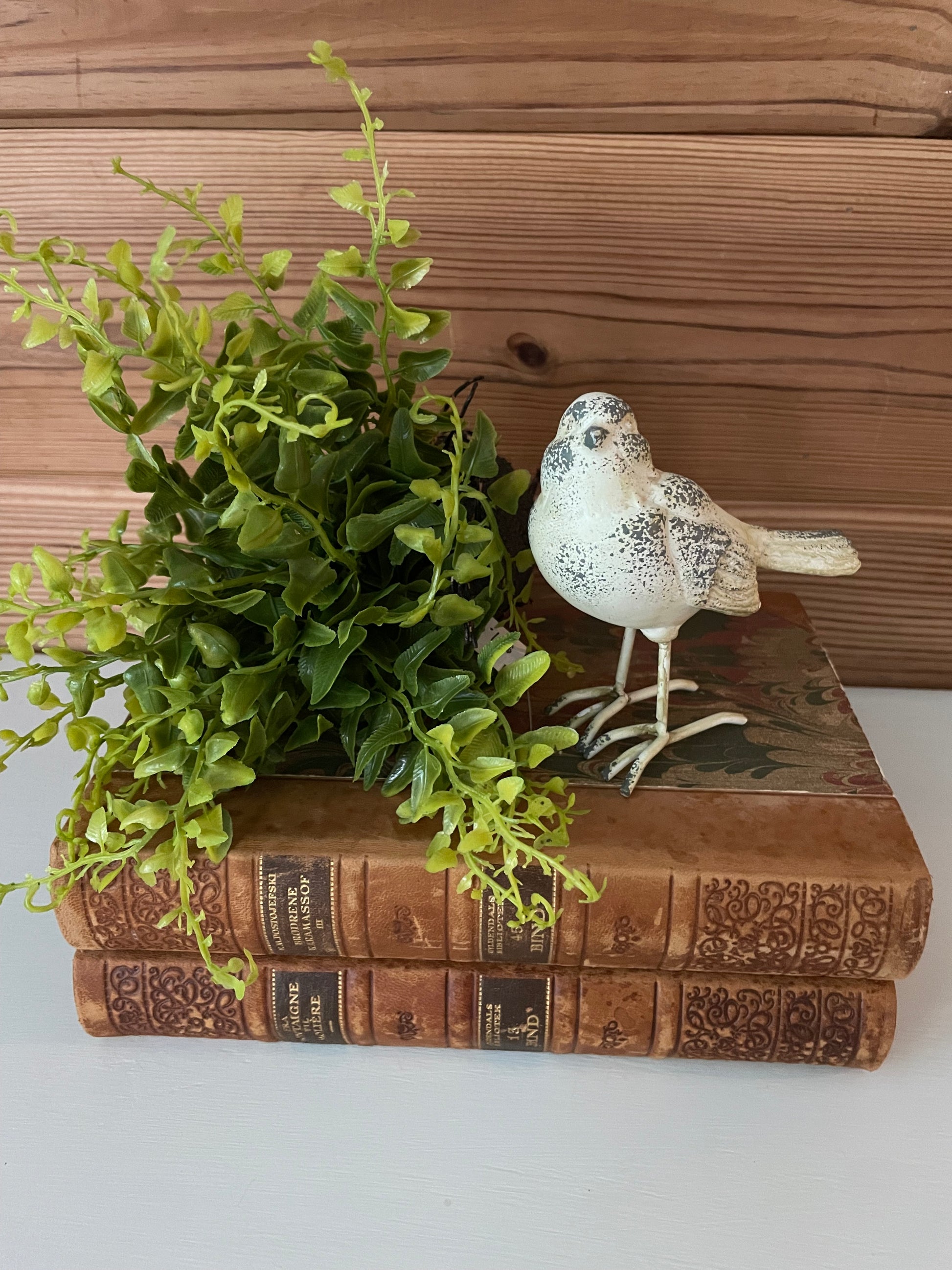 Resin metal bird decor in white/grey distressed finish, perched on vintage books with greenery. A charming home accent for rustic and farmhouse decor.