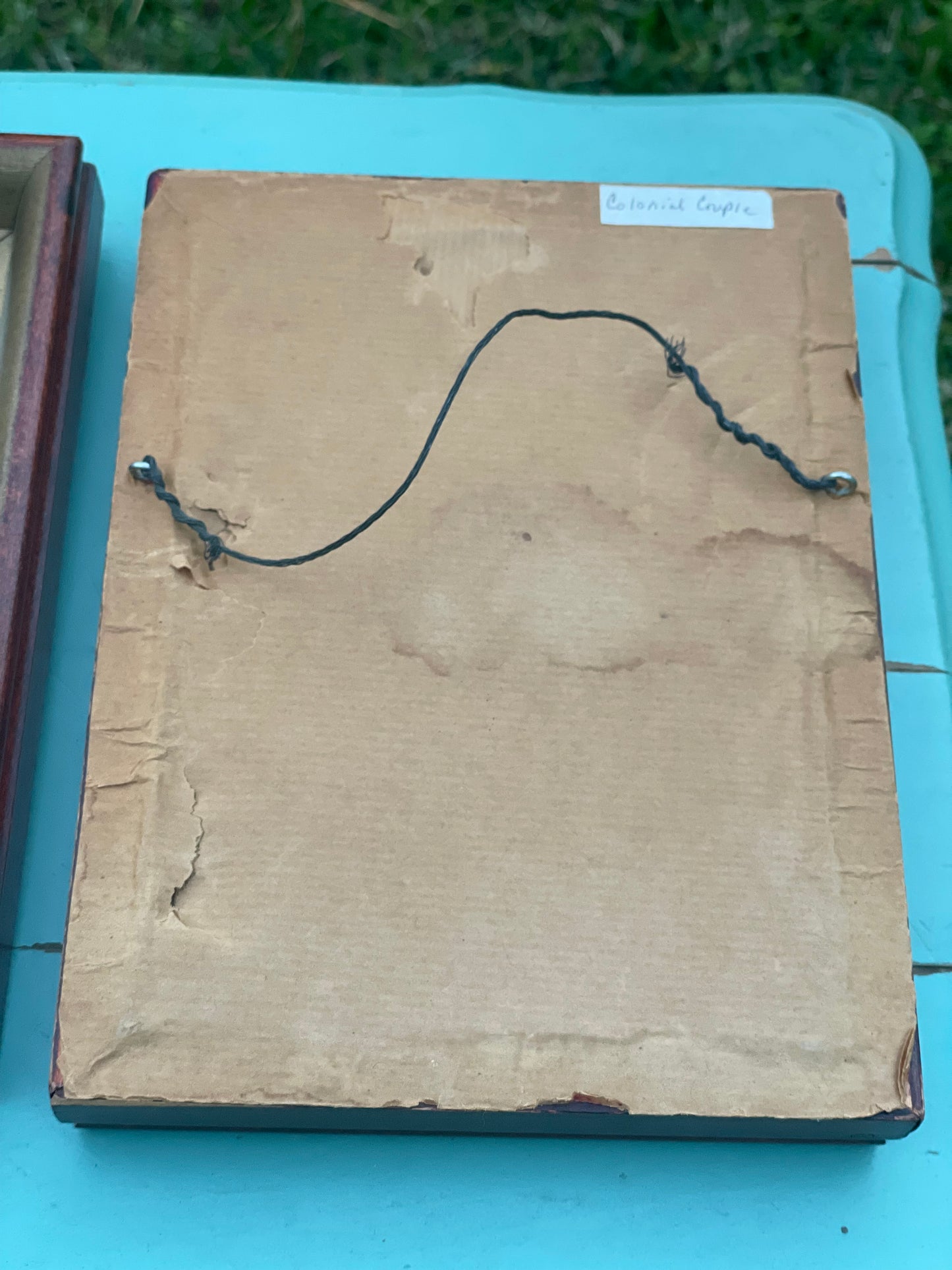 Back view of a framed Vintage Petite Pointe embroidery labeled 'Colonial Couple.' Aged paper backing with hanging wire for easy display.