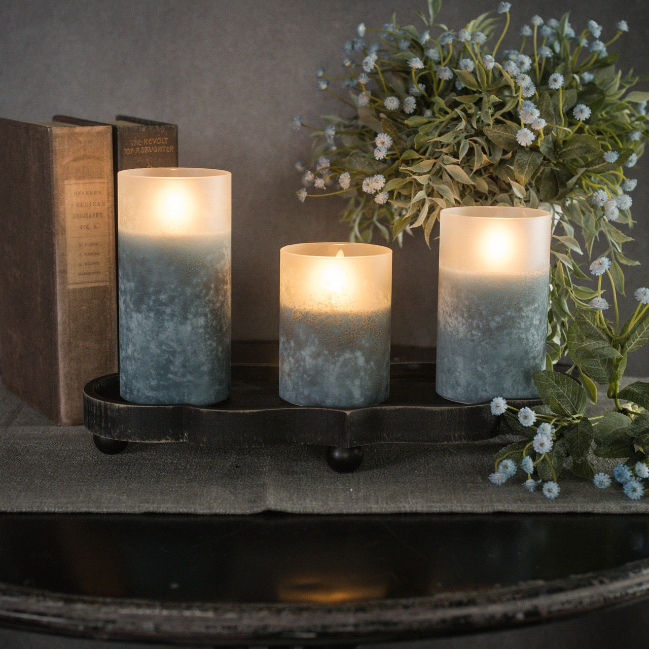 Set of three blue frosted glass 3D flame candles in varying sizes, beautifully arranged with books and floral decor for a serene glow.