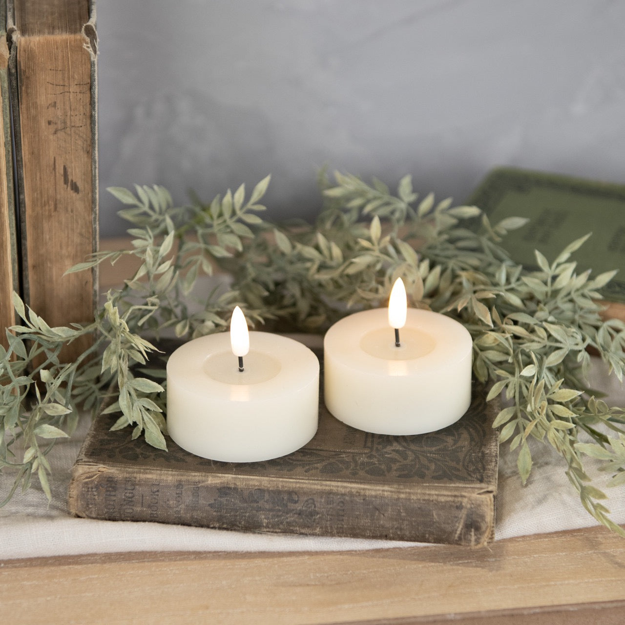 Pair of 3D flame oversized tealight candles on vintage books with greenery, creating a cozy and elegant home decor setting.