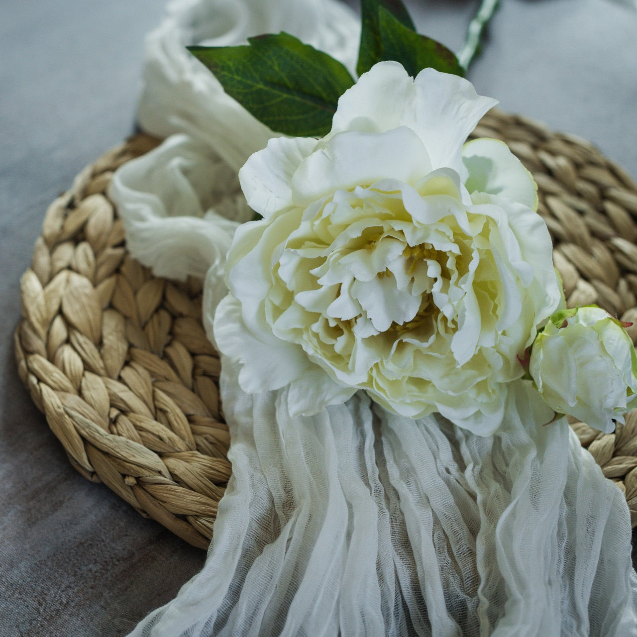 Elegant Cream Peony Spray 15-inch resting on woven mat with soft fabric. Lifelike artificial flower ideal for bouquets and home decor accents.