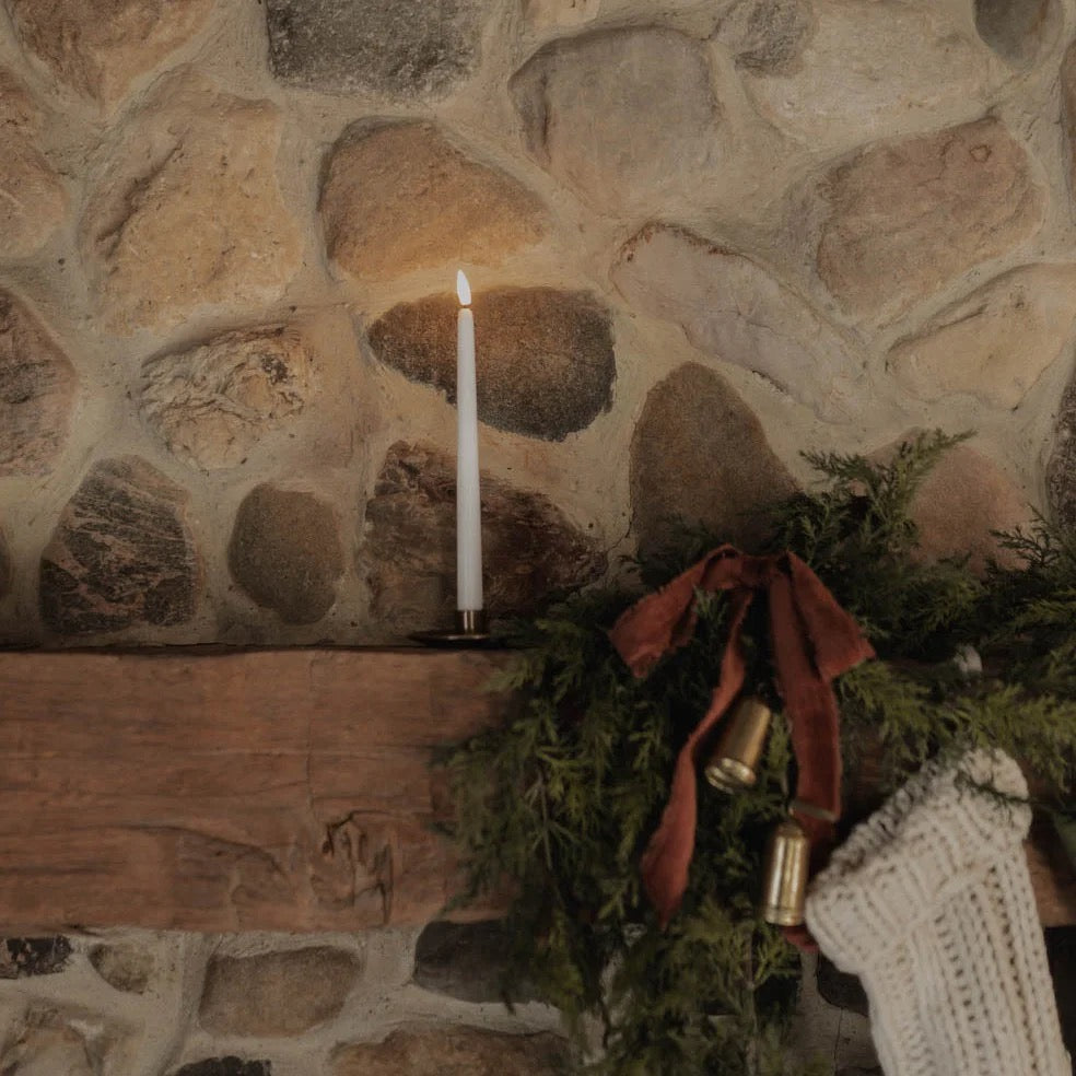 Antique Candle Co taper candle stand holding a lit candle on a rustic mantel. A warm and elegant home decor piece perfect for festive or cozy settings.