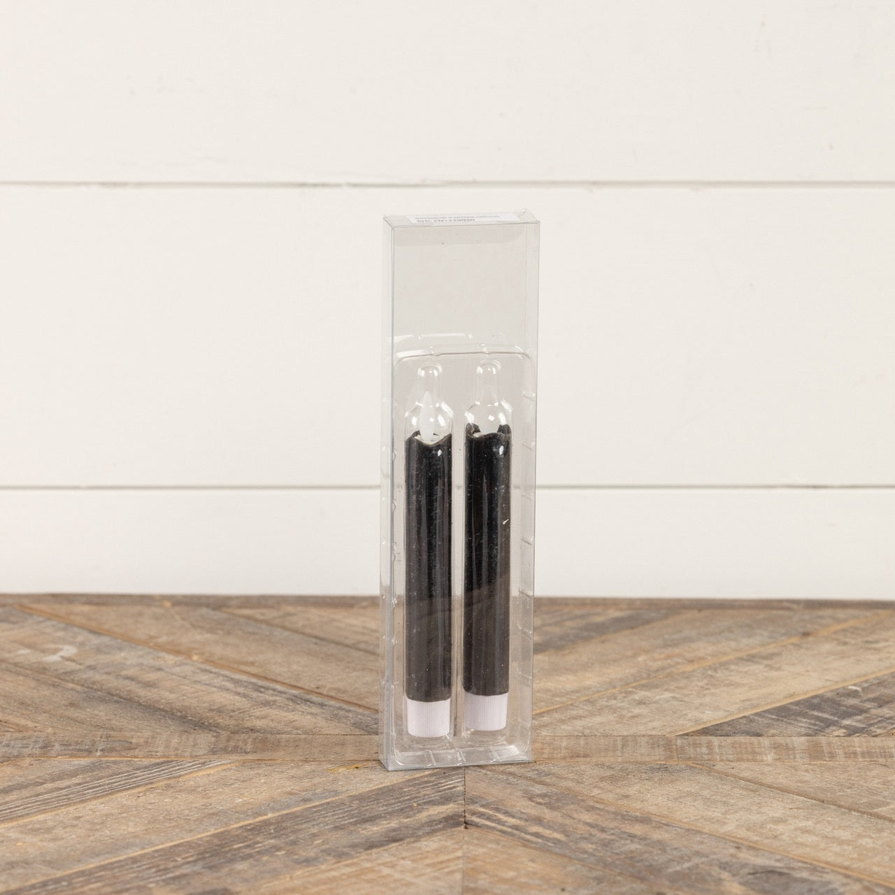 Packaged set of two 6.75-inch black taper candles with moving flame effect in a clear plastic case. Perfect for gifting or home decoration.