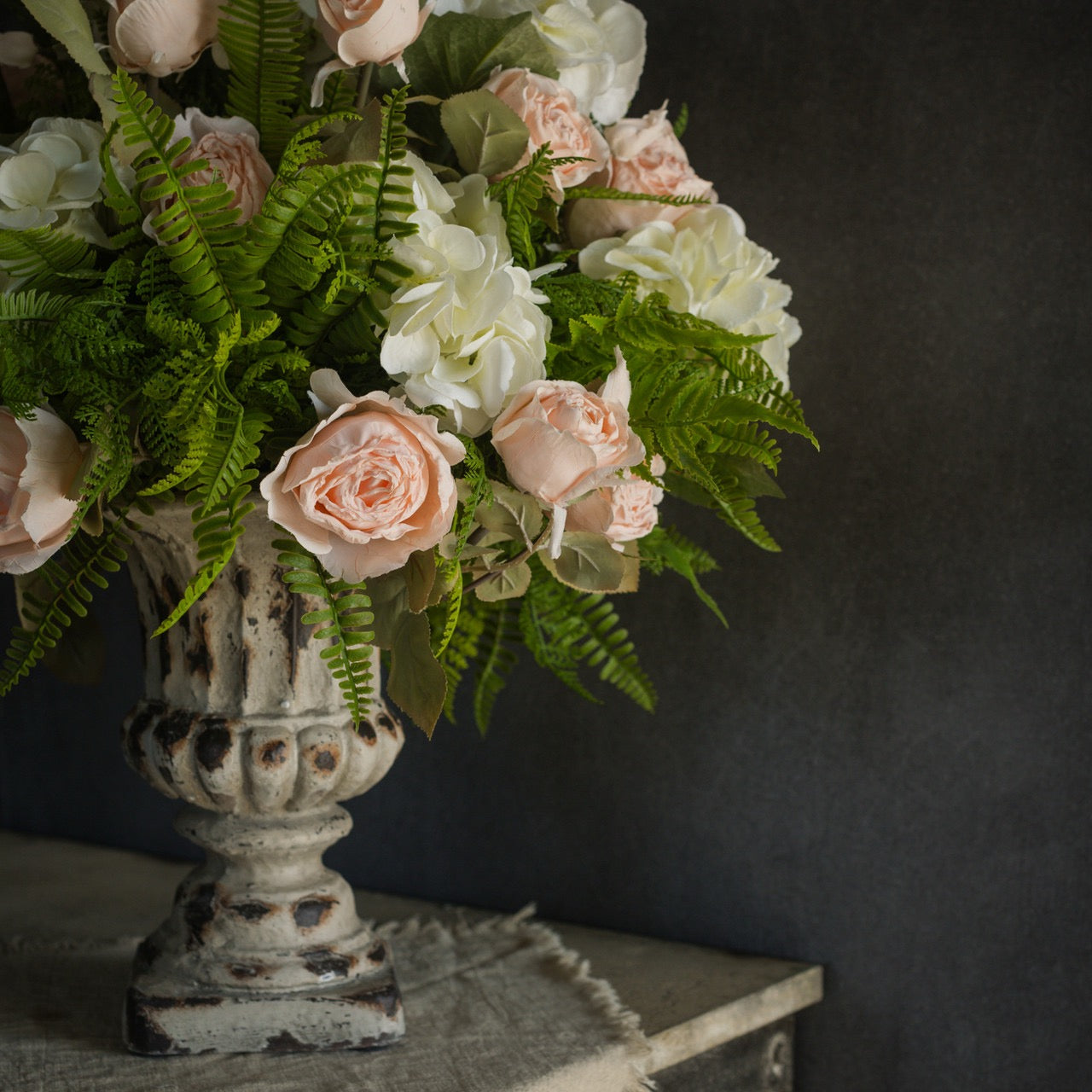 Artificial Sword Fern & Cedar Bush elegantly arranged with roses in a vintage urn. A stunning floral accent for home decor.