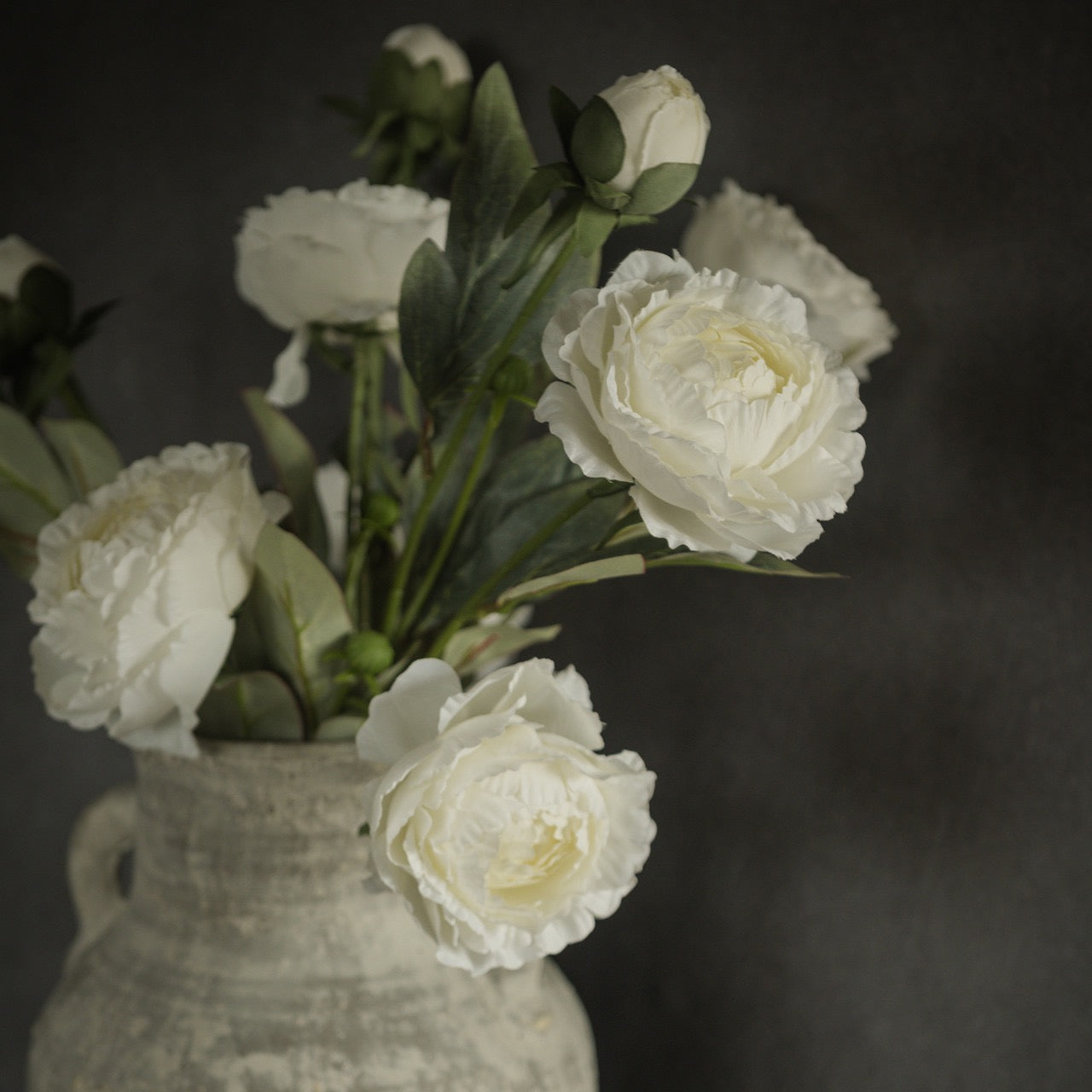 Artificial white peony spray in a rustic ceramic vase, featuring delicate, realistic blooms and green foliage for a timeless floral arrangement.