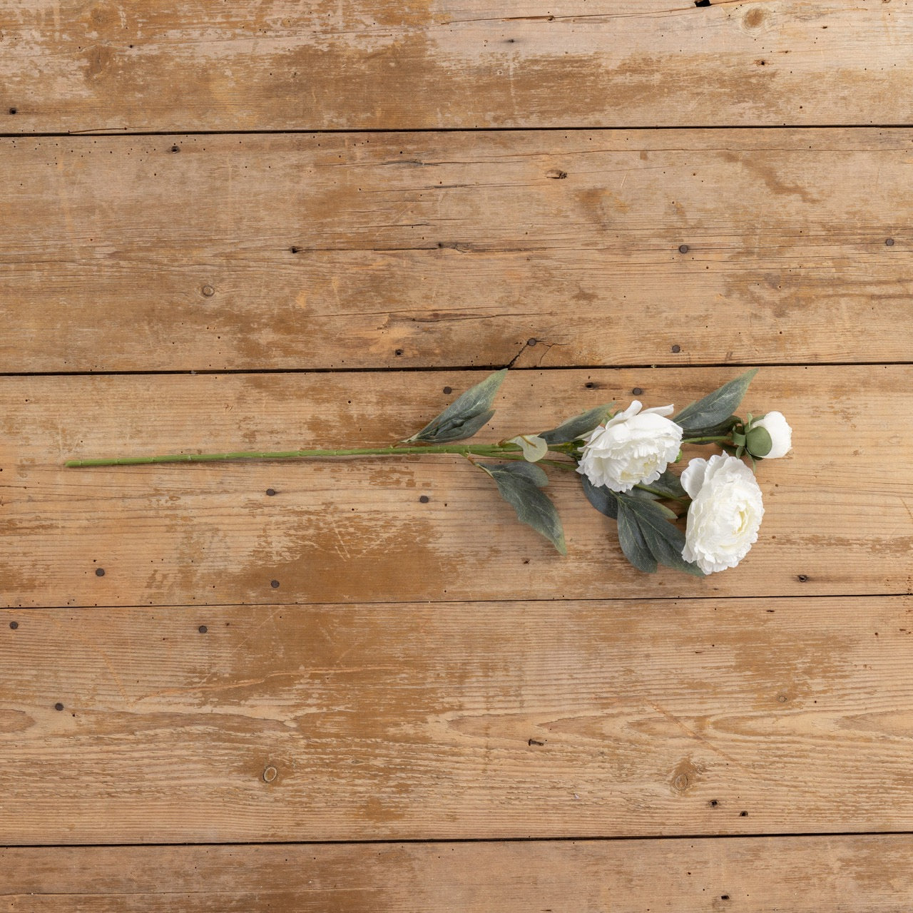 Single 27.5-inch white peony spray with detailed petals and green leaves, laid on a wooden surface, perfect for floral arrangements and home decor.