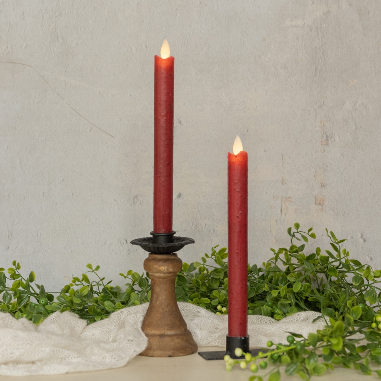 Set of two 9.5-inch moving flame red taper candles with a realistic flickering effect, perfect for home decor. Displayed with greenery and wooden accents.