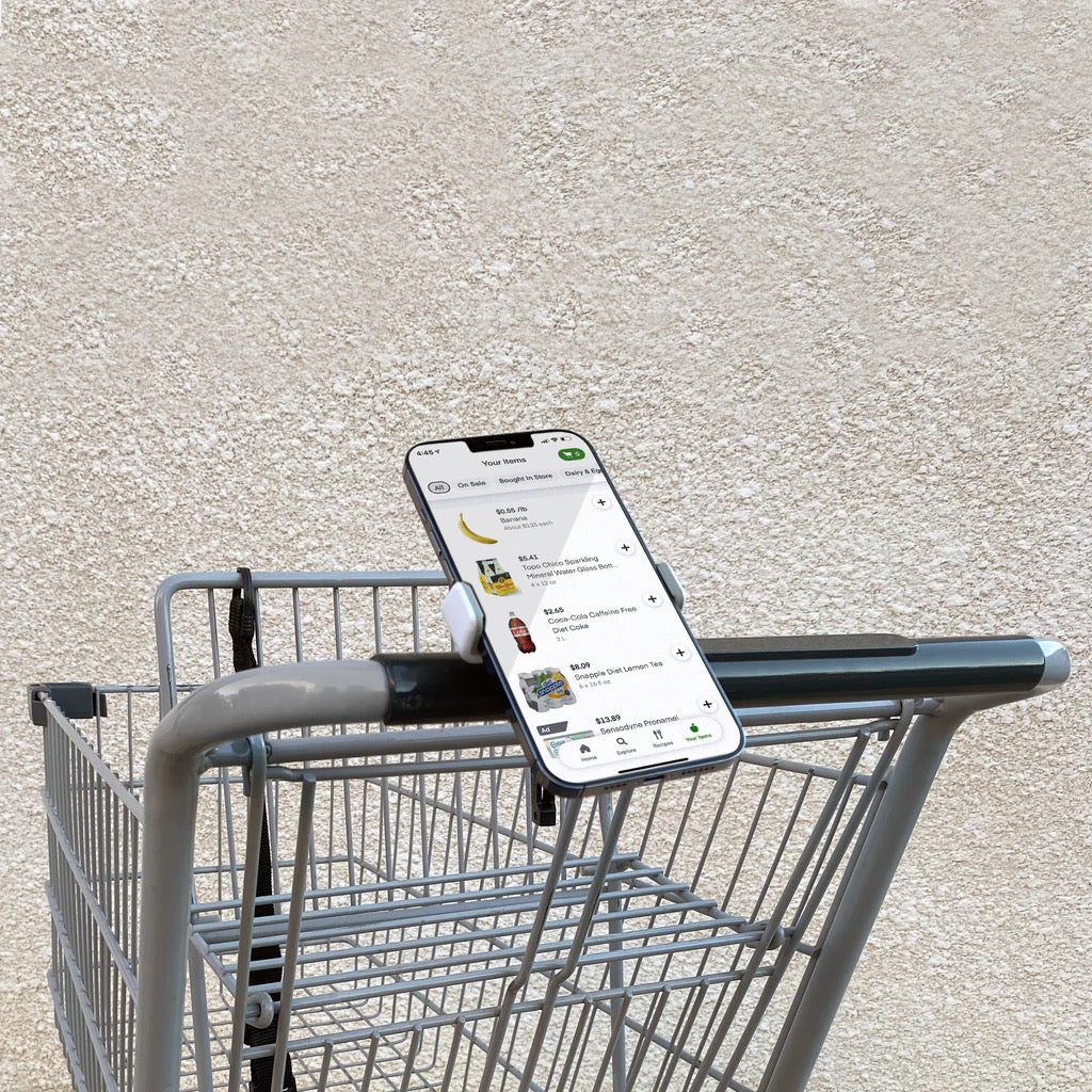 TECH CANDY ROLL WITH IT phone holder attached to a shopping cart handle, securely holding a smartphone for easy access while shopping.