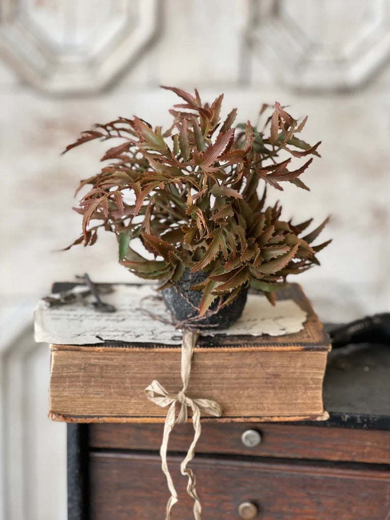 Rooted Frond - Fall 7 artificial plant with autumn-hued foliage in a rustic pot, placed on vintage books for a cozy home decor accent.