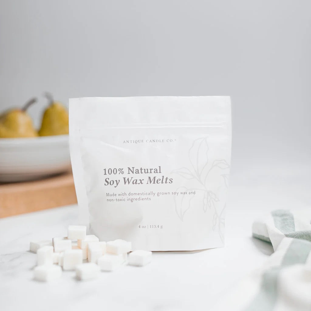 Antique Candle Co 100% natural soy wax melts in a white 4oz pouch, surrounded by small wax cubes on a marble surface. Clean, non-toxic home fragrance.