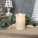 Flameless 5-inch moving flame cream candle with a wax finish, set in a festive holiday scene with greenery and white decorations. Ideal for cozy ambiance.