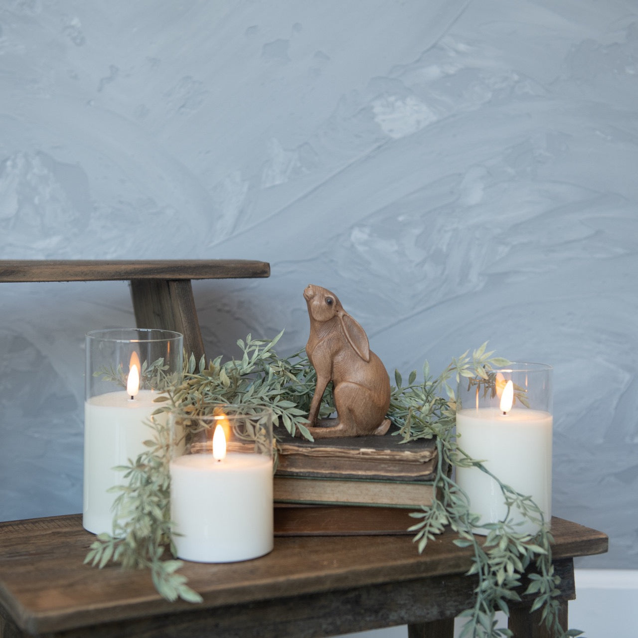 Ears Down Brown Bunny figurine displayed on stacked books with candles and greenery, creating a cozy and elegant home decor setting.