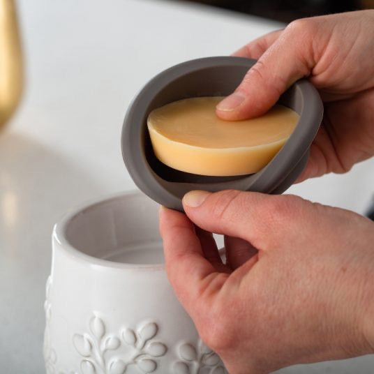 Close-up of hands placing a wax melt into the flip dish of a Gray Hobnail Flip Dish Wax Warmer. Convenient removable dish for easy wax replacement.