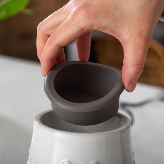 Hand lifting the flip dish from a Gray Hobnail Flip Dish Wax Warmer. Designed for mess-free wax removal and effortless fragrance changes.