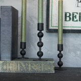 Set of black metal sculpted taper candlesticks with green candles, displayed on a decorative surface. Perfect for modern and vintage decor styles.