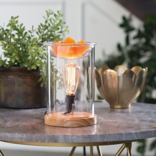 Wood and glass vintage bulb illumination fragrance warmer placed on a stylish table, melting orange wax cubes, enhancing home decor with warm lighting.