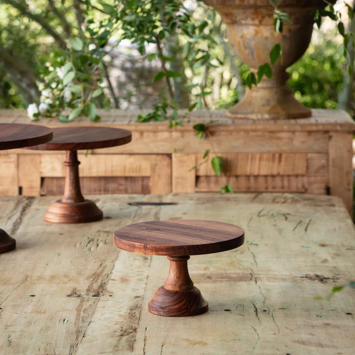 Set of wooden cake stands displayed on a rustic table, featuring a modern design with an olive oil finish. Perfect for stylish dessert presentation.