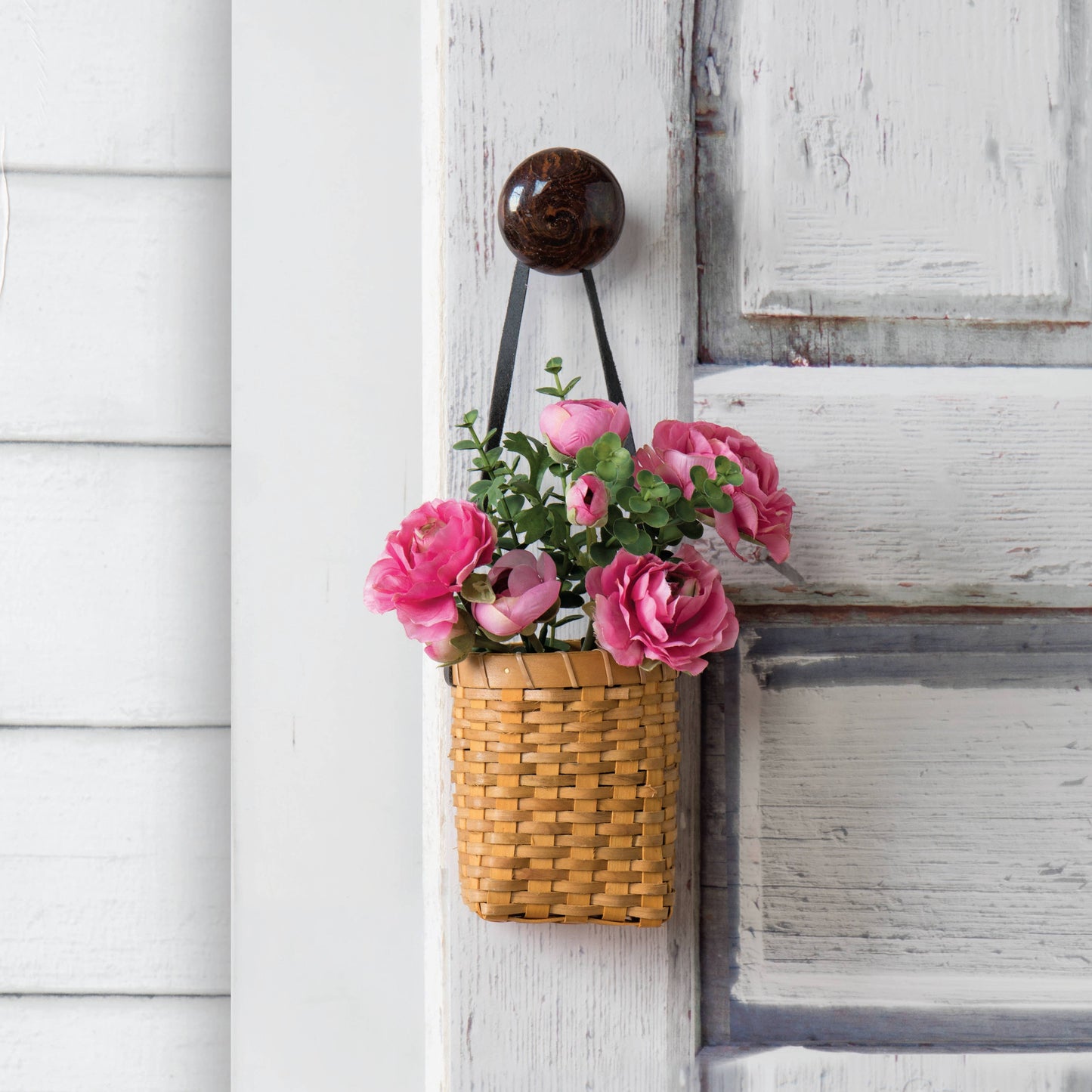 Oval Chipwood Hanging Planter displayed with pink flowers on a rustic door. Features a leather strap for easy hanging and a compact woven design.
