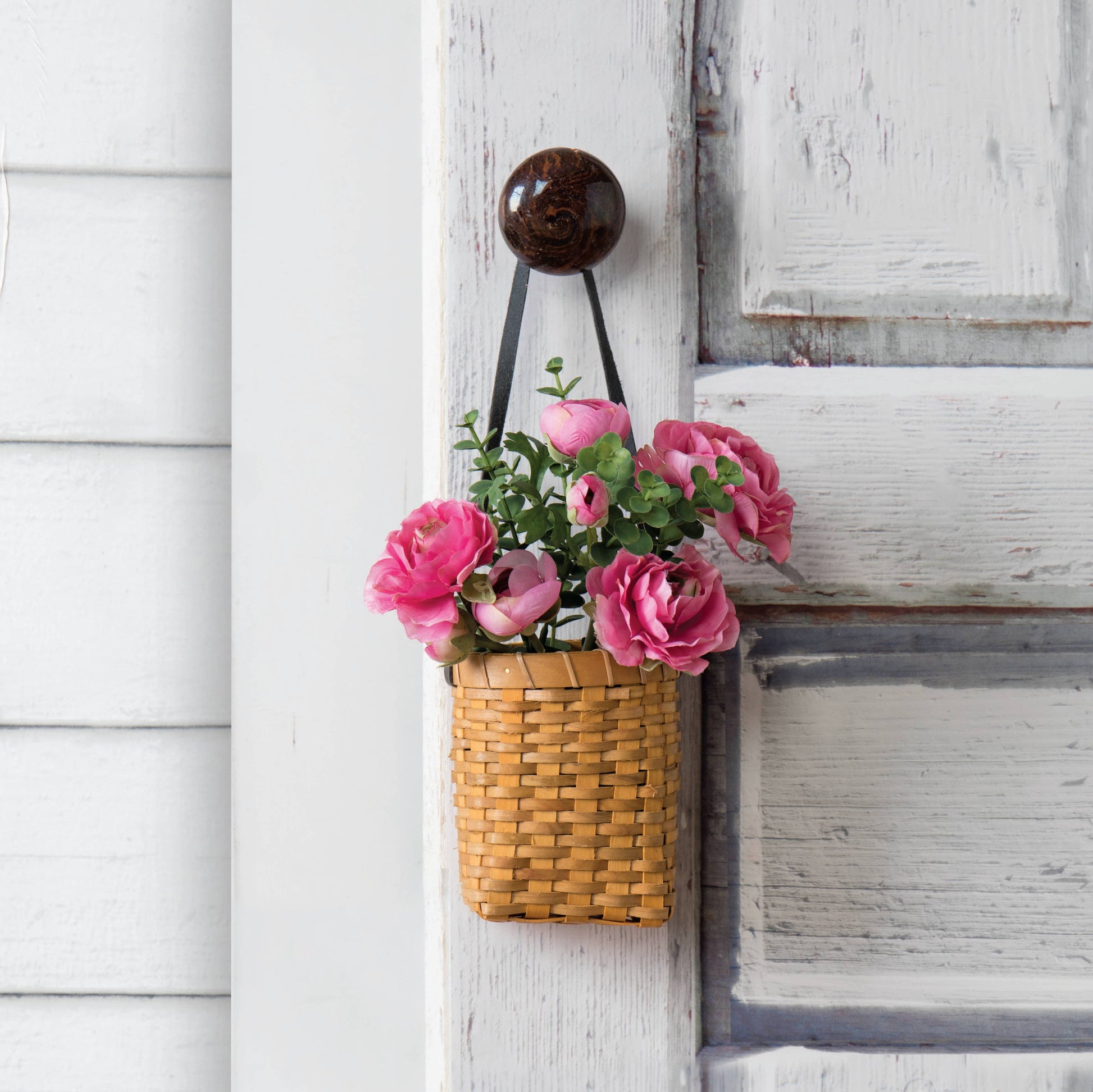 Oval Chipwood Hanging Planter displayed with pink flowers on a rustic door. Features a leather strap for easy hanging and a compact woven design.