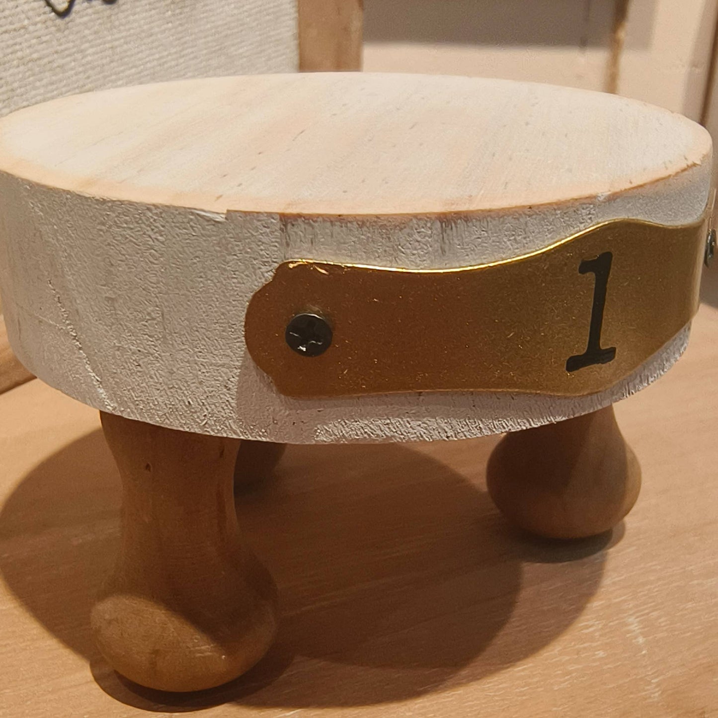 Close-up of a small white wooden display riser with a brass number plate and sturdy wooden legs, perfect for decorative displays.