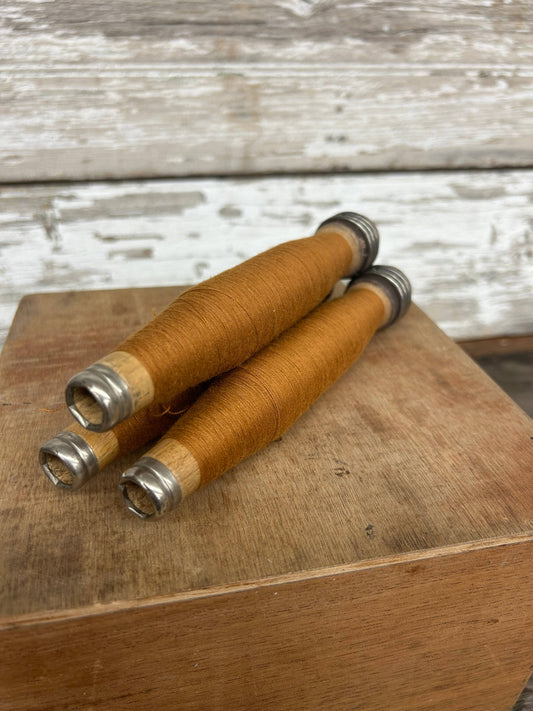 Set of three vintage copper yarn quills wrapped in copper-colored thread with metal tips, placed on a wooden surface. Ideal for home decor or crafting.