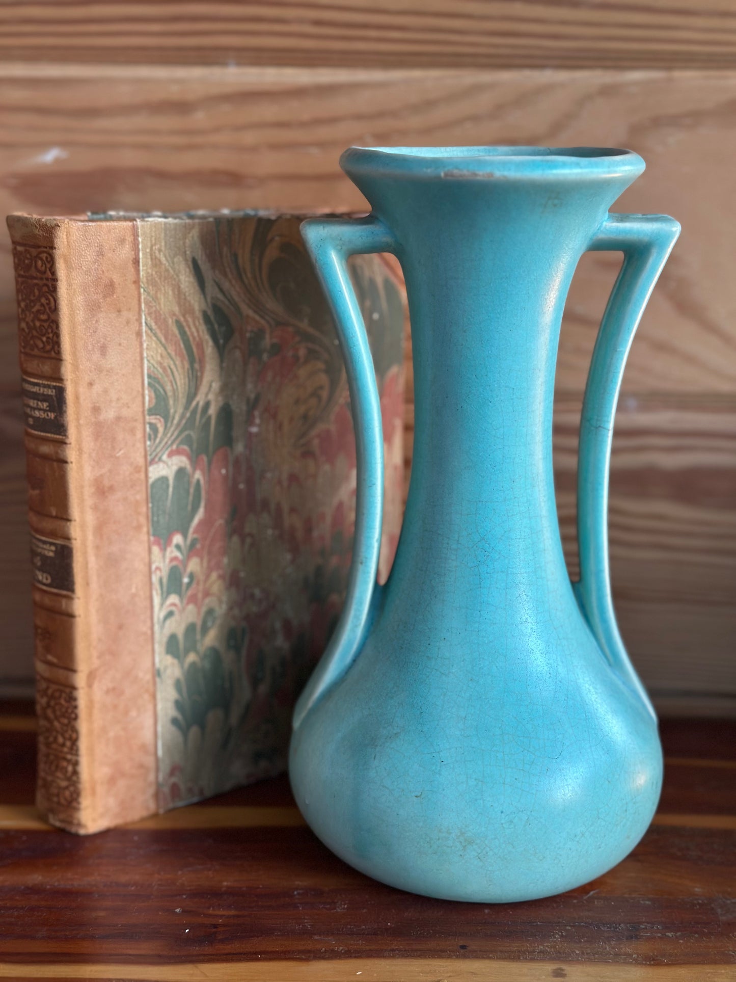 Mid-century vintage USA pottery vase in turquoise with a sleek, curved handle design. Shown beside an antique book for a timeless decor aesthetic.