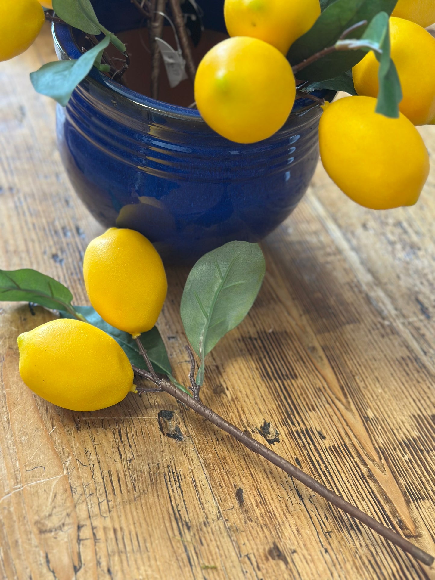 Artificial lemon floral pick with vibrant yellow lemons and green leaves placed on a wooden surface. Ideal for embellishments and decorative trims.