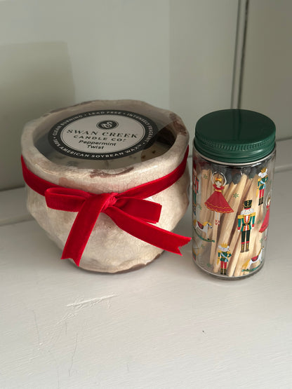 Jar candle with a red ribbon and a container of matches on a white surface