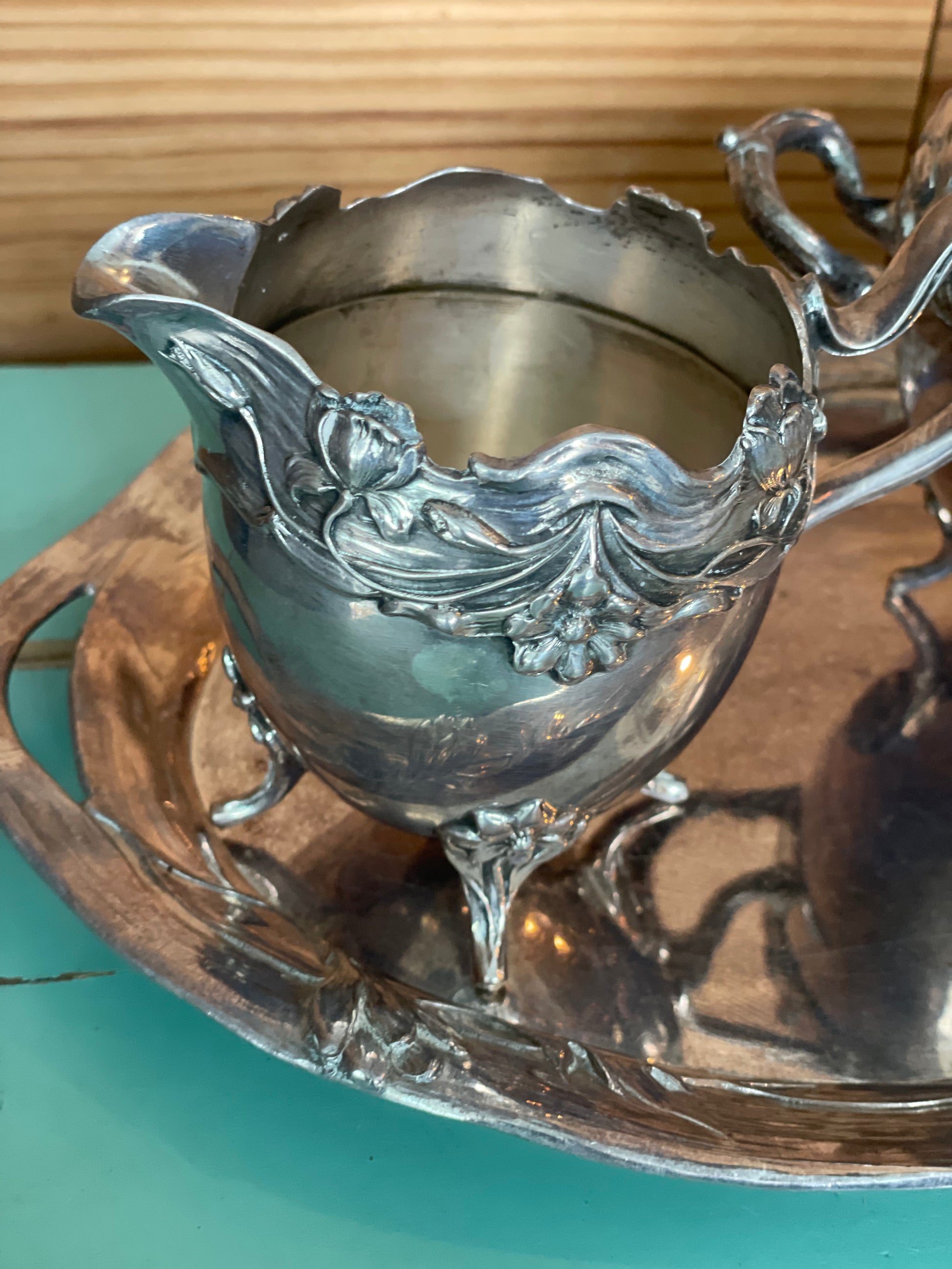 Close-up of vintage silver-plated creamer with intricate floral engravings and elegant curved legs. A perfect piece for classic serveware collections.