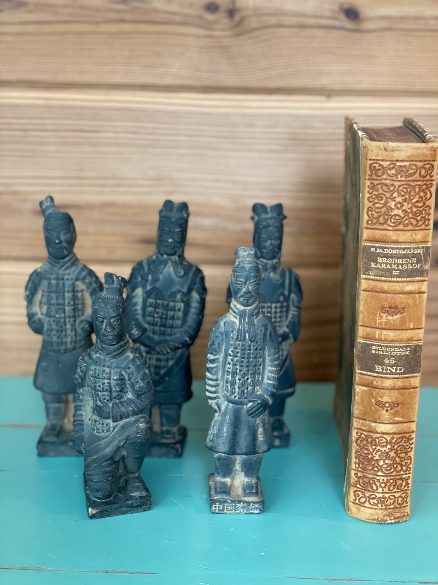 Set of five vintage terracotta Chinese warrior figurines displayed next to an antique book. Hand-painted sculptures showcasing intricate historical details.