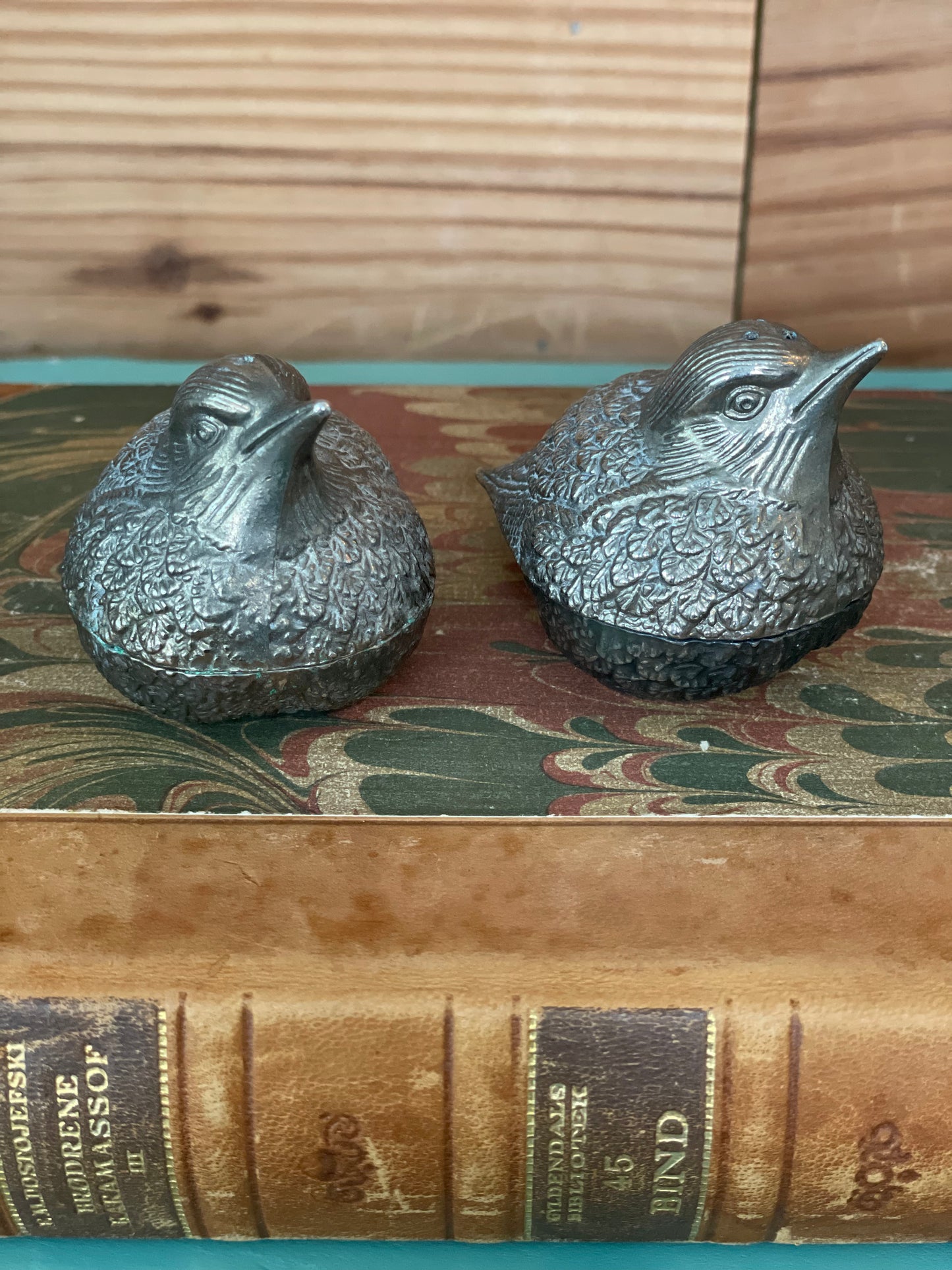 Vintage silver-plated bird-shaped salt and pepper shakers with intricate detailing, placed on an antique book. Elegant tableware for classic dining decor.