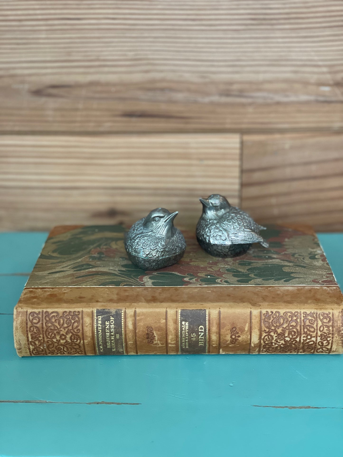 Ornate silver-plated bird salt and pepper shakers resting on a vintage book. A timeless and elegant accent for kitchen and dining table settings.