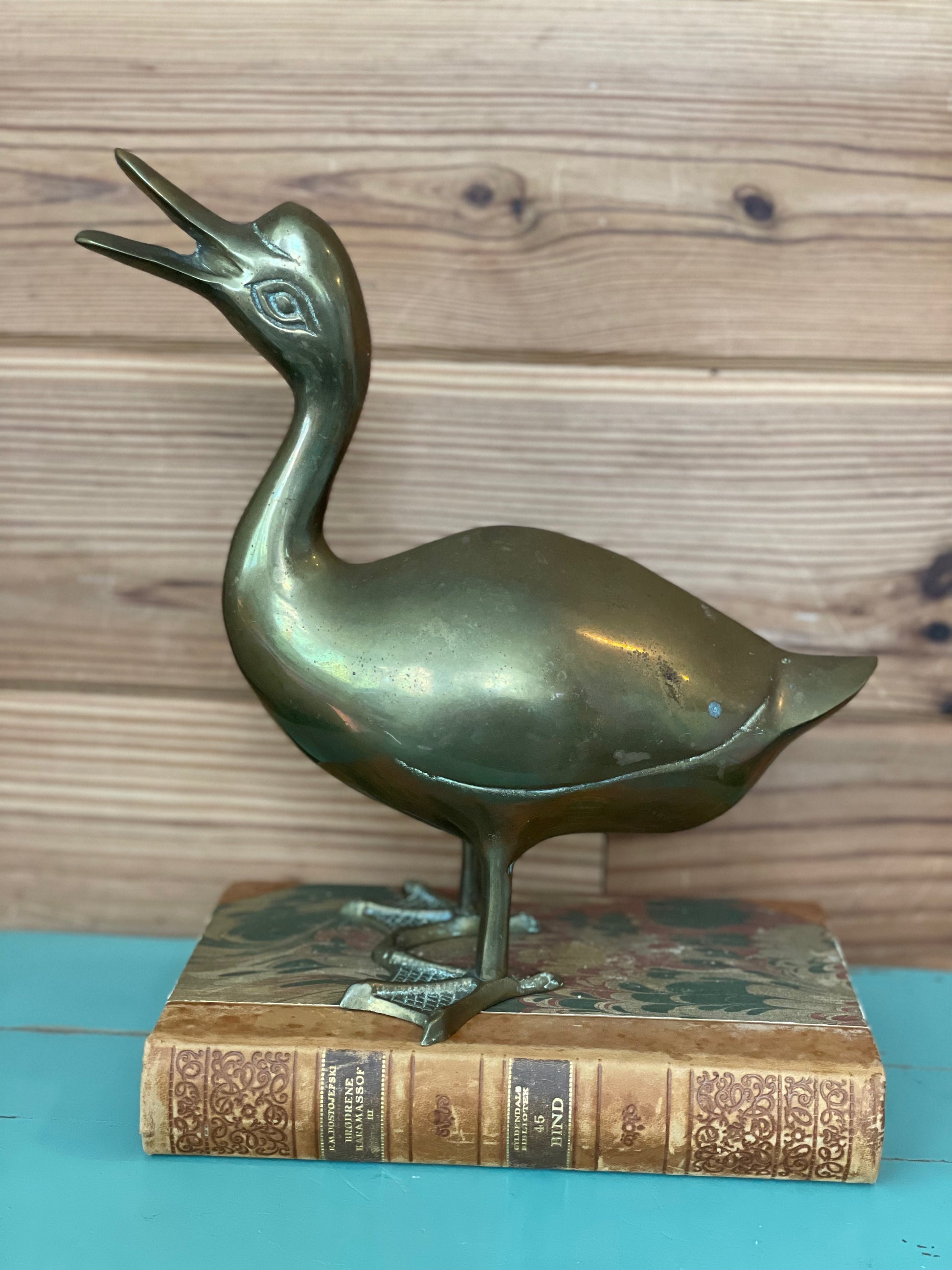 Vintage brass duck sculpture with a patina finish, perched on an antique book. A charming decorative piece for collectors and home decor enthusiasts.