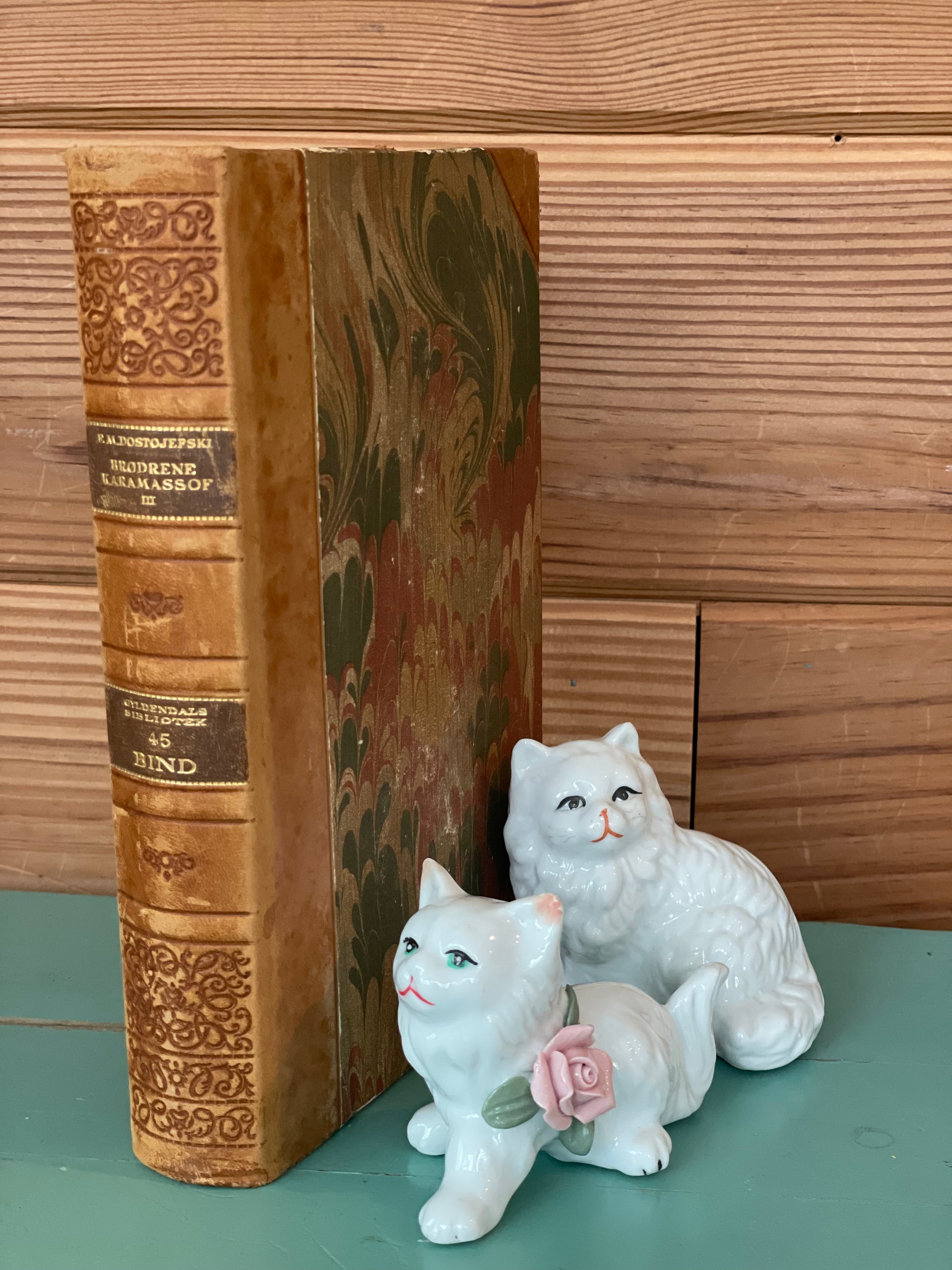 Vintage ceramic cat figurines displayed beside an antique book. A unique decorative piece for classic and vintage-inspired interiors.