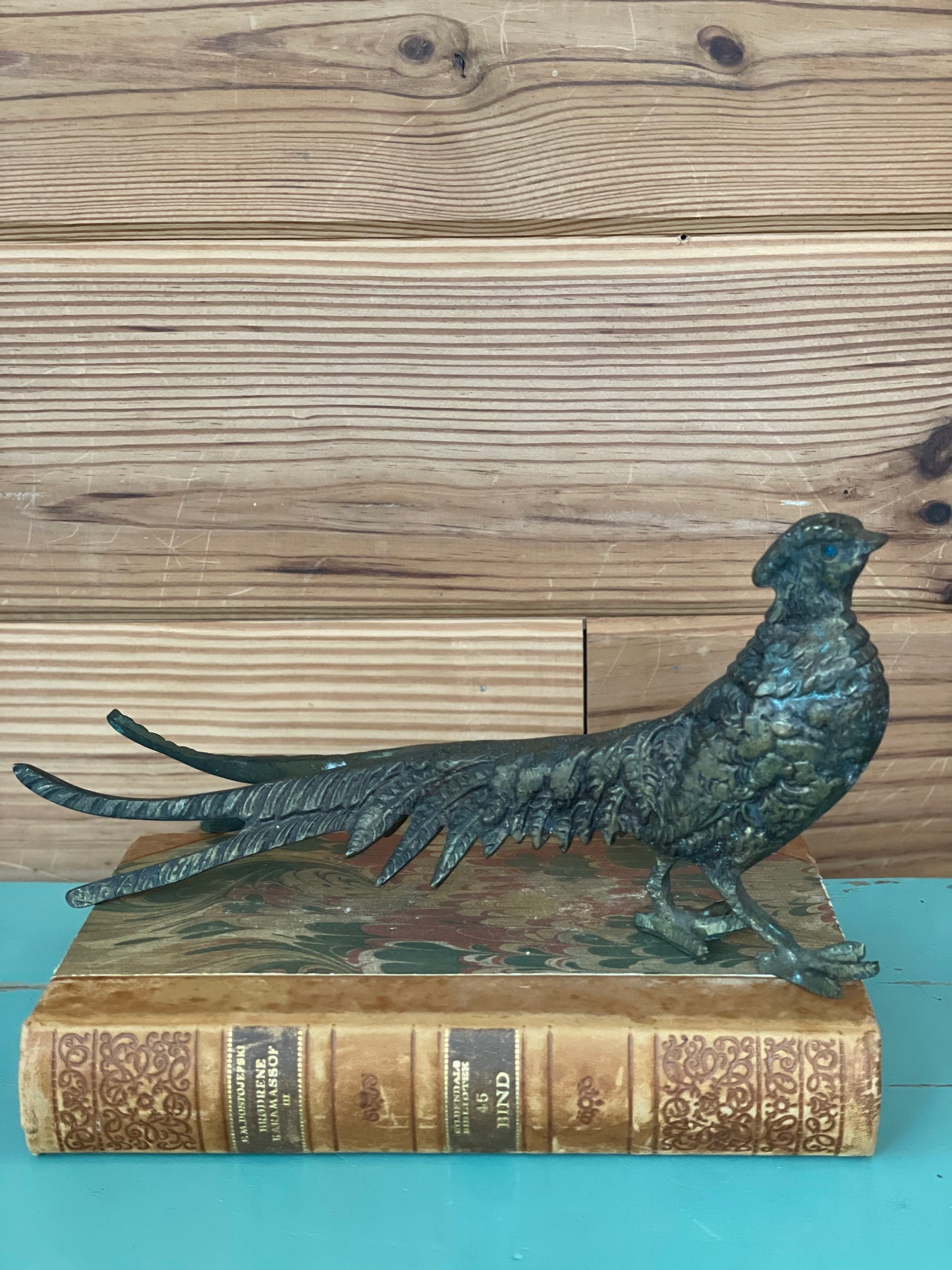 Elegant vintage brass pheasant statue resting atop an antique book. A timeless decorative piece for classic and vintage-inspired interiors.