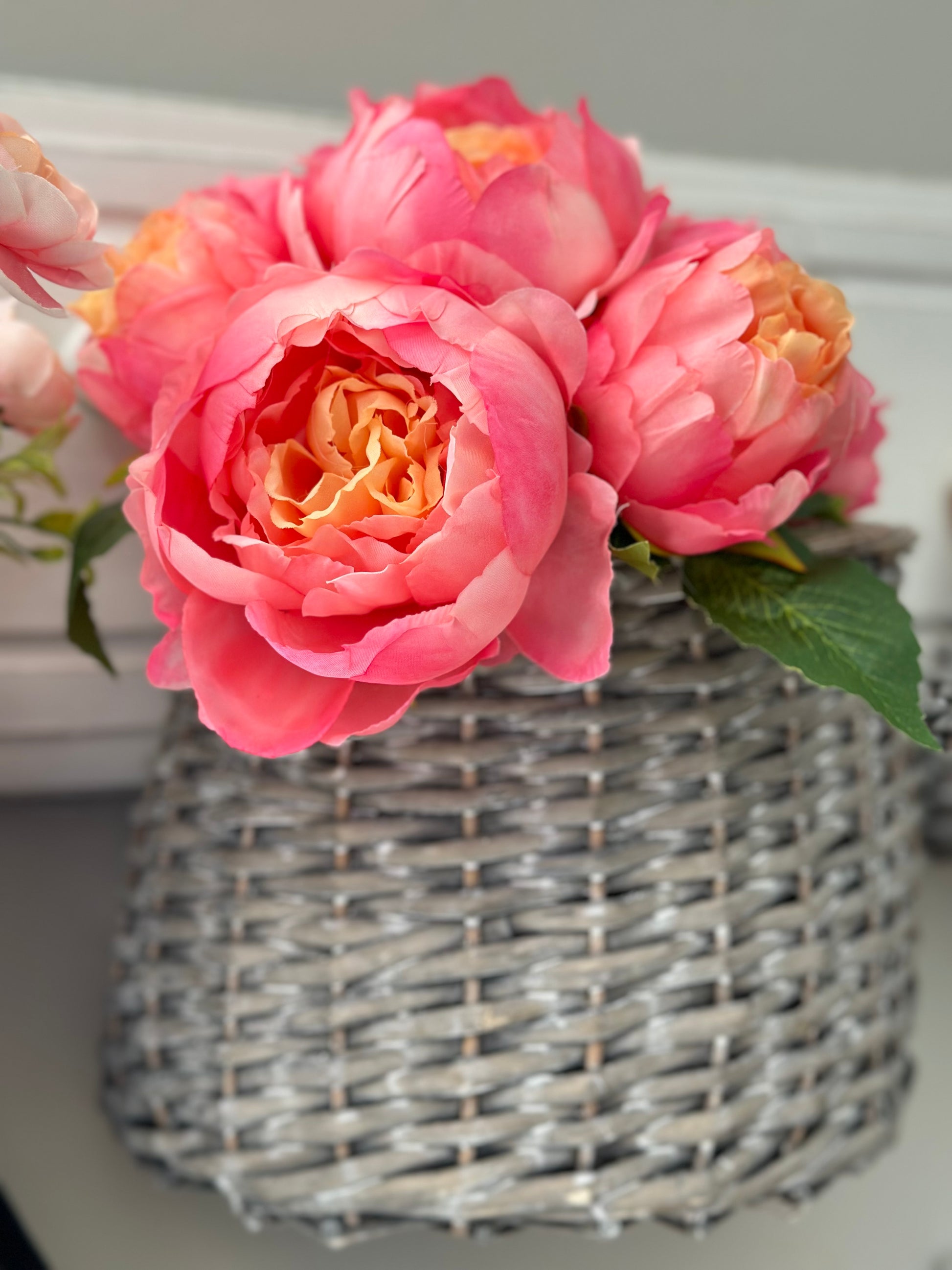 Gray woven basket storage with pink peonies, perfect for home decor and organization. Stylish and versatile for any interior setting.