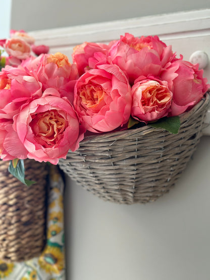 Gray wicker storage basket filled with vibrant pink peonies, hanging on a white hook. A decorative and functional home organization solution.