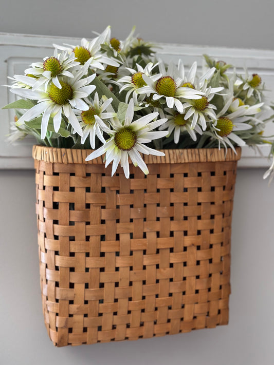 Hanging brown chip basket with woven design, filled with white daisies. A stylish and durable home decor piece for organizing or displaying flowers.