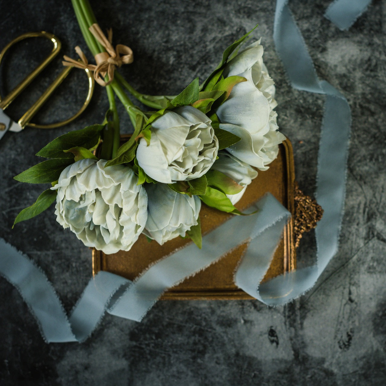 Dusty Blue Peony Bundle placed on a vintage gold box with ribbon and scissors. Realistic artificial flowers ideal for elegant floral arrangements.