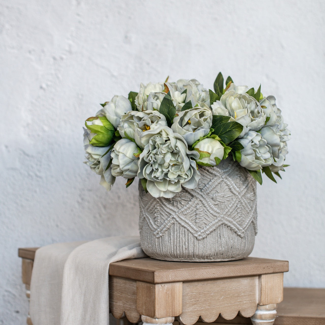 Dusty Blue Peony Bundle arranged in a textured ceramic vase on a wooden table. Elegant artificial floral decor for home and event styling.